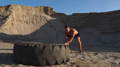Muscle-athlete-strongman-man-hits-a-hammer-on-a-huge-wheel-in-the-sandy-mountains-in-slow-motion.-strength-and-endurance-training-for-wrestlers