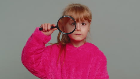 Curious-preteen-child-girl-kid-holding-magnifying-glass-near-face-funny-eye-searching-analysing