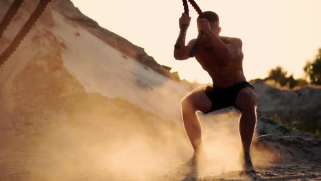 Athletic-man-on-exercise-around-the-sand-hills-at-sunset-hits-the-rope-on-the-ground-and-raised-the-dust.