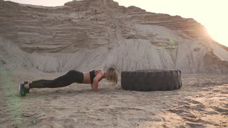 Girl-on-sand-quarry-jumping-burpee-with-push-UPS-through-the-wheel-in-the-sand