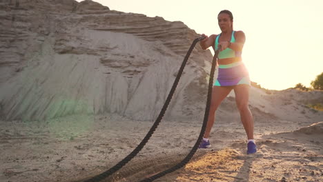 Female-athlete-training-outdoors-around-the-sand-hills-at-sunset.-Active-physical-activity-workout.-crossfit.-The-girl-has-a-rope-on-the-ground