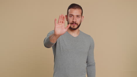 Young-man-say-No-hold-palm-folded-crossed-hands-in-stop-gesture-warning-of-finish-prohibited-access