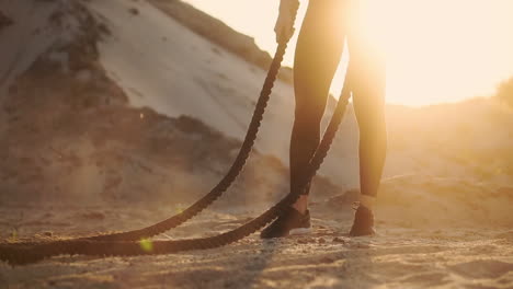 Sporty-woman-training-around-the-sand-hills-at-sunset-hits-the-rope-on-the-ground-and-raised-the-dust.