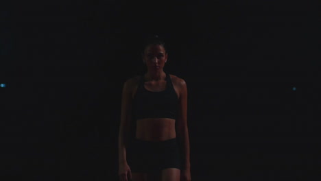 Professional-woman-athlete-on-a-dark-background-gotovtes-to-run-the-sprint-of-Jogging-shoes-in-sneakers-on-the-track-of-the-stadium-on-a-dark-background.-Average-plan