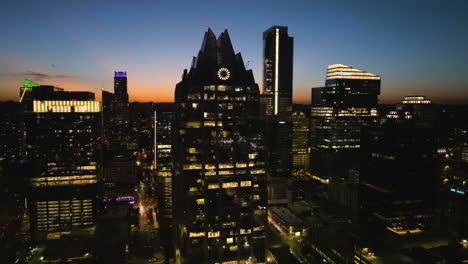 Aerial-view-rising-around-the-Illuminated-Frost-bank-tower,-dusk-in-Austin,-USA