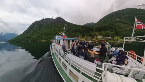 Tourist-boat-passing-a-small-remote-settlement-without-road-in-Fjaerlandsfjorden-Norway---Handheld-wide-angle-showing-both-boat-with-tourists-and-small-settlement-in-background