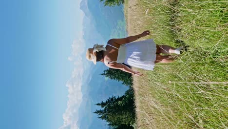 Vertical-shot-of-cute-woman-walking-through-green-grass-on-hill-in-Austria-during-summer---following-shot
