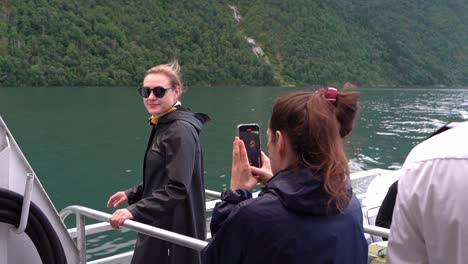 Touristin-Dreht-Sich-Lächelnd-Um,-Als-Eine-Freundin-Sie-An-Bord-Einer-Bootsfahrt-Im-Norwegischen-Fjord-Fotografiert-–-Zeitlupe