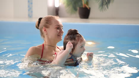 Young-mom-in-the-pool-playing-with-her-baby-daughter-in-slow-motion.-Sports-family-engaged-in-an-active-lifestyle