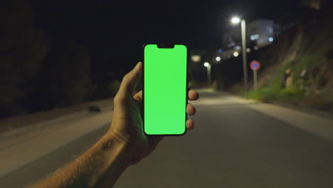 Engaging-Nighttime-POV:-Man's-Hand-Holds-iPhone-14-with-Greenscreen-on-Empty-Street-Lit-by-Lamps,-Chroma-key