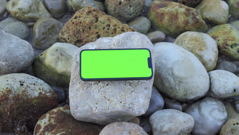 iPhone-14-with-Green-Screen-Resting-on-Rocks-by-the-Morning-Sea