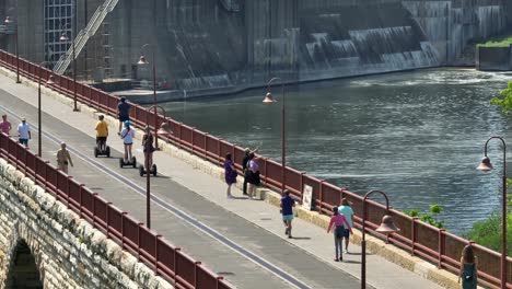 People-walk,-run,-go-sightseeing,-and-ride-segways-on-pedestrian-bridge-in-Minneapolis