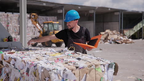 Man-in-hardhat-inspects-paper-bale-at-outdoor-recycling-plant,-slomo