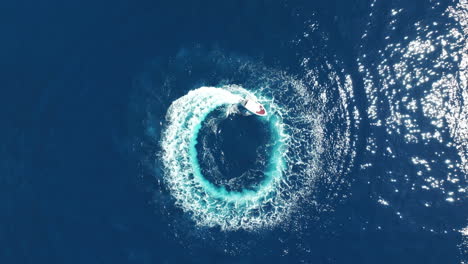 Top-Down-Aerial-View-of-Motor-Boat-Spinning-in-Circle-in-Deep-Blue-Sea-Water,-High-Angle-Drone-Shot