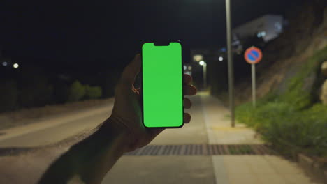 Engaging-Nighttime-POV:-Man's-Hand-Holds-iPhone-14-with-Greenscreen-on-Empty-Street-Lit-by-Lamps,-Chroma-key