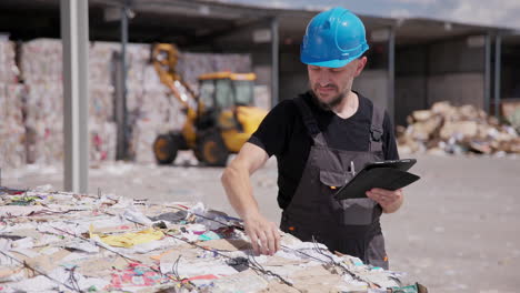 Recycling-plant-worker-uses-tablet-while-inspecting-bale-of-paper,-pan