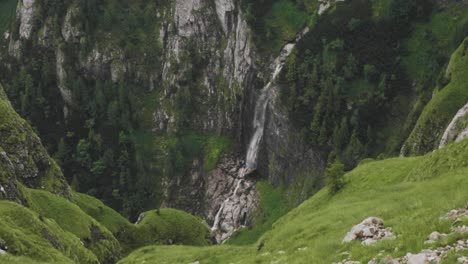 Slow-motion-static-shot-of-a-waterfall-pouring-into-a-mountain-valley-with-an-alpine-landscape
