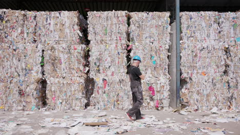 Male-worker-inspects-paper-bales-at-recycling-facility,-wide-slomo
