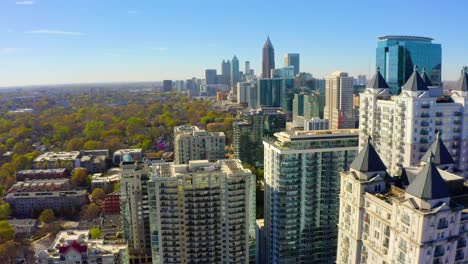 Aerial-drone-shot-slowly-flying-forward-over-residential-buildings-near-Piedmont-Park-in-Midtown-looking-toward-the-skyscrapers-in-downtown-Atlanta,-Georgia-on-a-sunny-day-with-blue-skies