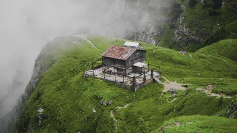 Slow-motion-panning-right-shot-of-an-old-wooden-chalet-placed-on-a-mountain-cliff-with-mist-in-the-background