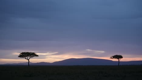 Beautiful-Night-Time-Landscape-of-Africa-Savanna-and-Acacia-Trees-in-Masai-Mara-in-Kenya,-Dark-Blue-Moody-Dramatic-Stormy-African-Sky-at-Nighttime-in-Rainy-Season,-Background-with-Copy-Space