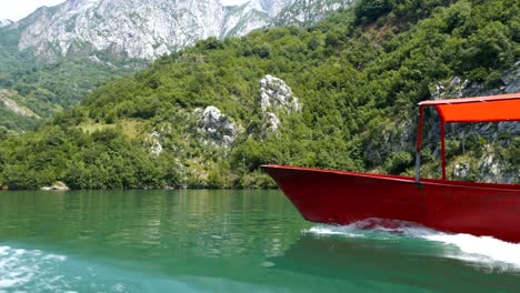 Albania,-Lake-Koman,-bow-of-a-red-ferry-on-the-lake's-surface,-with-the-Accursed-Mountains-in-the-background