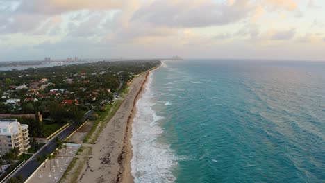 Aerial-drone-shot-hovering-above-Palm-Beach-island-as-the-Atlantic-Ocean-waves-crash-against-the-beach-and-the-sunrise-lights-up-the-sky
