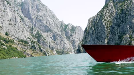 Albania,-Lake-Koman,-prow-of-a-red-boat-on-the-lake's-surface,-with-the-Accursed-Mountains-in-the-background
