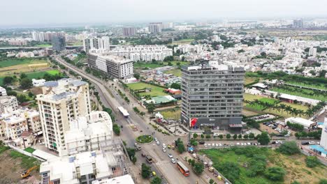Scene-of-ring-road-passing-through-Rajkot-city-surrounded-by-high-rise-buildings,-low-rise-buildings-visible-in-the-background,-aerial-view-of-skyscraper-building-in-Rajkot-city