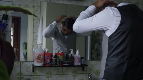 Man-in-suit-preparing-his-hair-in-front-of-big-mirror-in-the-bathroom