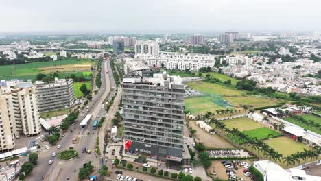 Aerial-view-of-Rajkot-City's-Skyscraper-Building,-very-heavy-traffic-can-be-seen-on-the-ring-road,-very-few-buildings-visible-on-either-side-of-the-road