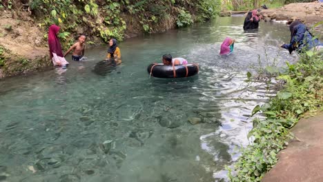 children-swimming-in-a-clear-spring-river-using-deep-wheeled-floats-in-Kali-Mudal-Gumuk