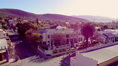 An-enchanting-aerial-view-captures-a-Montagu-hotel-from-the-front,-nestled-against-a-backdrop-of-majestic-mountains-and-rolling-hills,-offering-a-serene-escape