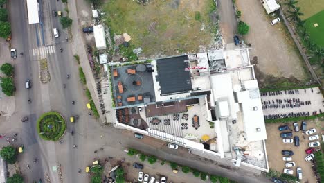 Top-view-of-terrace-garden-restaurant,-aerial-view-of-skyscraper-building-in-Rajkot-city,-camera-panning-down-and-vehicles-passing-on-the-road-can-be-seen