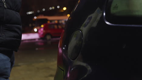 Side-view-of-man-opening-gas-cap-cover-lid-of-car-to-pump-petrol-on-cold-night