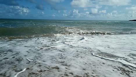 Slow-motion-ocean-waves-splashing-onto-scenic-sandy-island-beach-blue-sky-soothing-tranquil-coastline