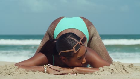 A-young-African-girl-kneels-in-the-white-sand-of-a-Caribbean-beach-in-a-green-bikini