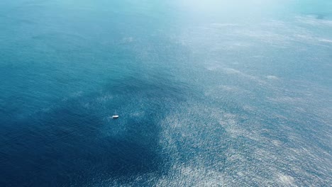 Aerial-Distant-View-of-Sailboat-looking-very-small-in-a-Vast-Blue-Ocean-with-some-clouds-overhead-in-South-Pacific-Ocean