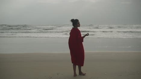 POV-Shot:-Woman-dressed-in-red-looking-at-the-sea-with-curiosity-in-the-evening-as-winds-blow-her-dress-she-turns-around