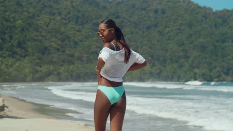 Ein-Mädchen-In-Einem-Breen-Bikini-Und-Einem-Netztop-Spaziert-An-Einem-Weißen-Sandstrand-Mit-Meereswellen-Im-Hintergrund