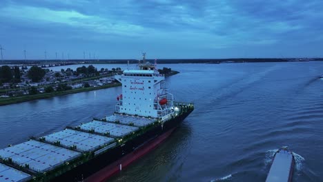 As-light-fades-over-the-river-Dortsche-Kil-a-large-container-ship-sails-onwards,-aerial