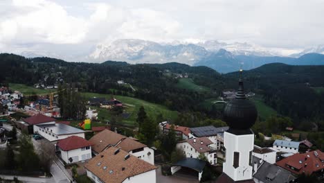 Drone-shot-flying-by-the-church-in-Oberbozen,-Italy-to-reveal-the-looming-mountainous-landscape