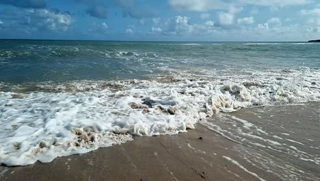 Slow-motion-ocean-waves-splashing-onto-scenic-sandy-island-beach-soothing-blue-sky-tranquil-coastline