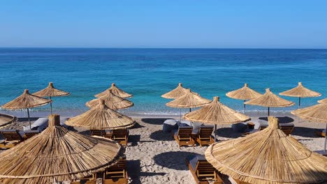Blaues-Türkisfarbenes-Meer-Und-Klarer-Himmel-An-Einem-Sonnigen-Sommerurlaubstag-Am-Ruhigen-Strand-Mit-Liegestühlen-Und-Sonnenschirmen,-Ionische-Küste-Albaniens
