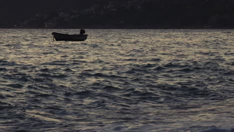 Fishing-boat-anchored-near-shoreline-of-Mediterranean-village,-floating-on-shallow-lagoon-at-dusk,-sea-waves-splashing-on-bay