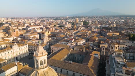 Amazing-Aerial-View-of-Domed-Cathedral-in-Catania,-Italy-with-Famous-Mount-Etna-Volcano-in-Background
