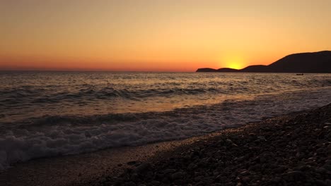 Goldene-Stunde-In-Einer-Wunderschönen-Bucht-Mit-Orangefarbenem-Himmel,-Der-Sich-Im-Meer-Spiegelt,-Und-Sonnenuntergang-Hinter-Den-Silhouetten-Der-Berge-An-Der-Ionischen-Küste-Albaniens