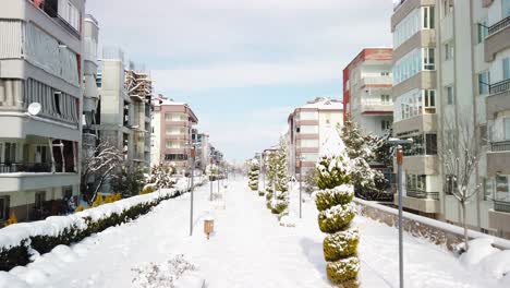 Low-to-high-drone-like-shot-on-a-cloudy-day-in-Denizli,-Turkey,-with-snow-covered-landscape,-apartment-buildings-on-both-sides,-and-a-pedestrian-walkway-resembling-a-park-in-between