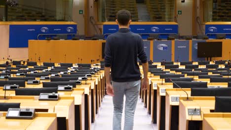 Hombre-Caminando-Dentro-De-La-Sala-Plenaria-Vacía-Del-Parlamento-Europeo-Y-Sentándose-En-Una-Silla