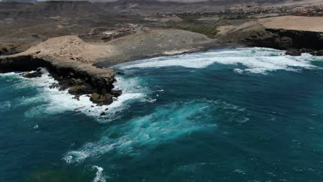 La-Pared-beach,-Fuerteventura:-aerial-view-traveling-out-over-the-beach-and-the-rock-formation-that-is-there,-on-the-island-of-Fuerteventura-on-a-sunny-day